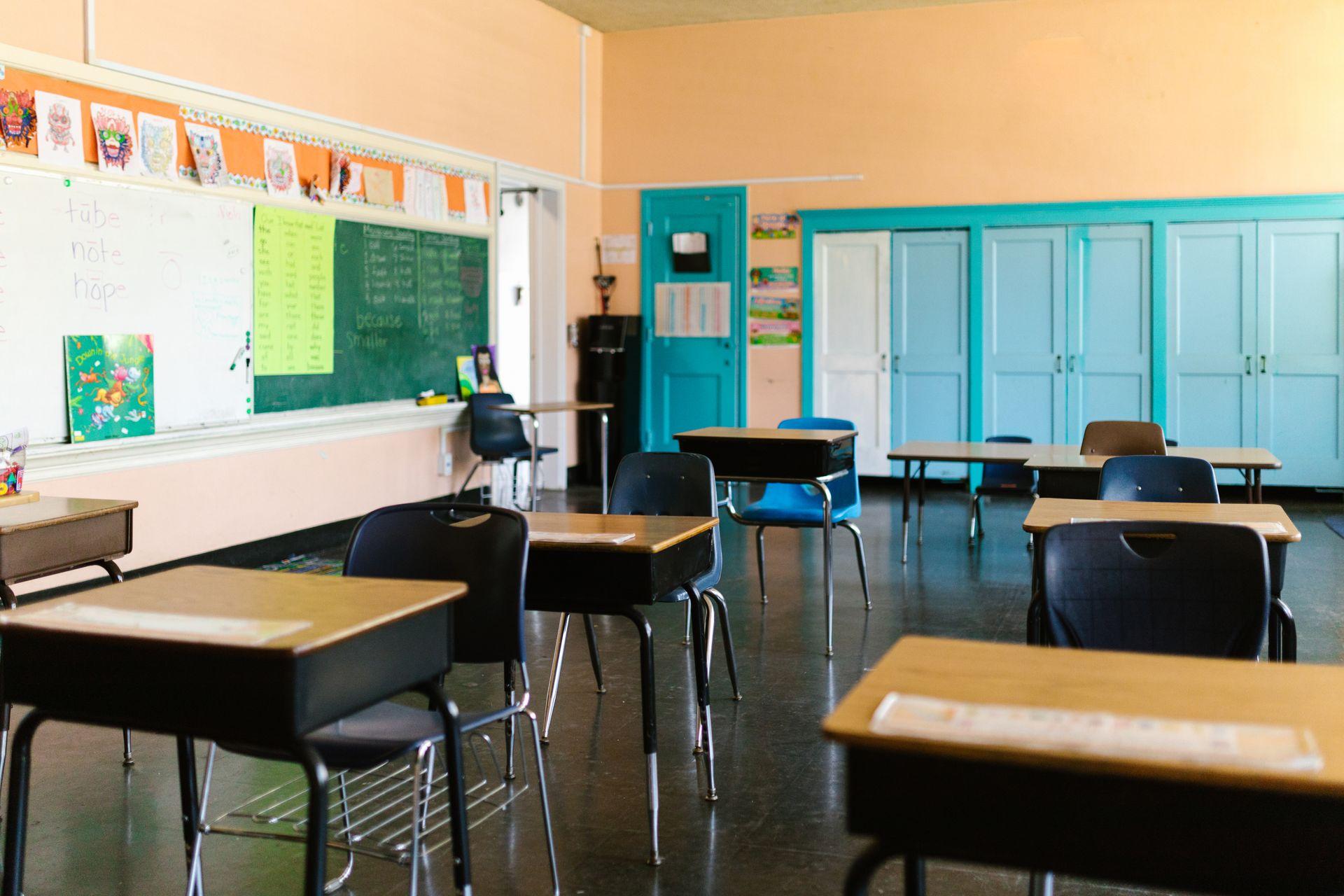 Sala de aula vazia com carteiras, quadro e materiais na parede