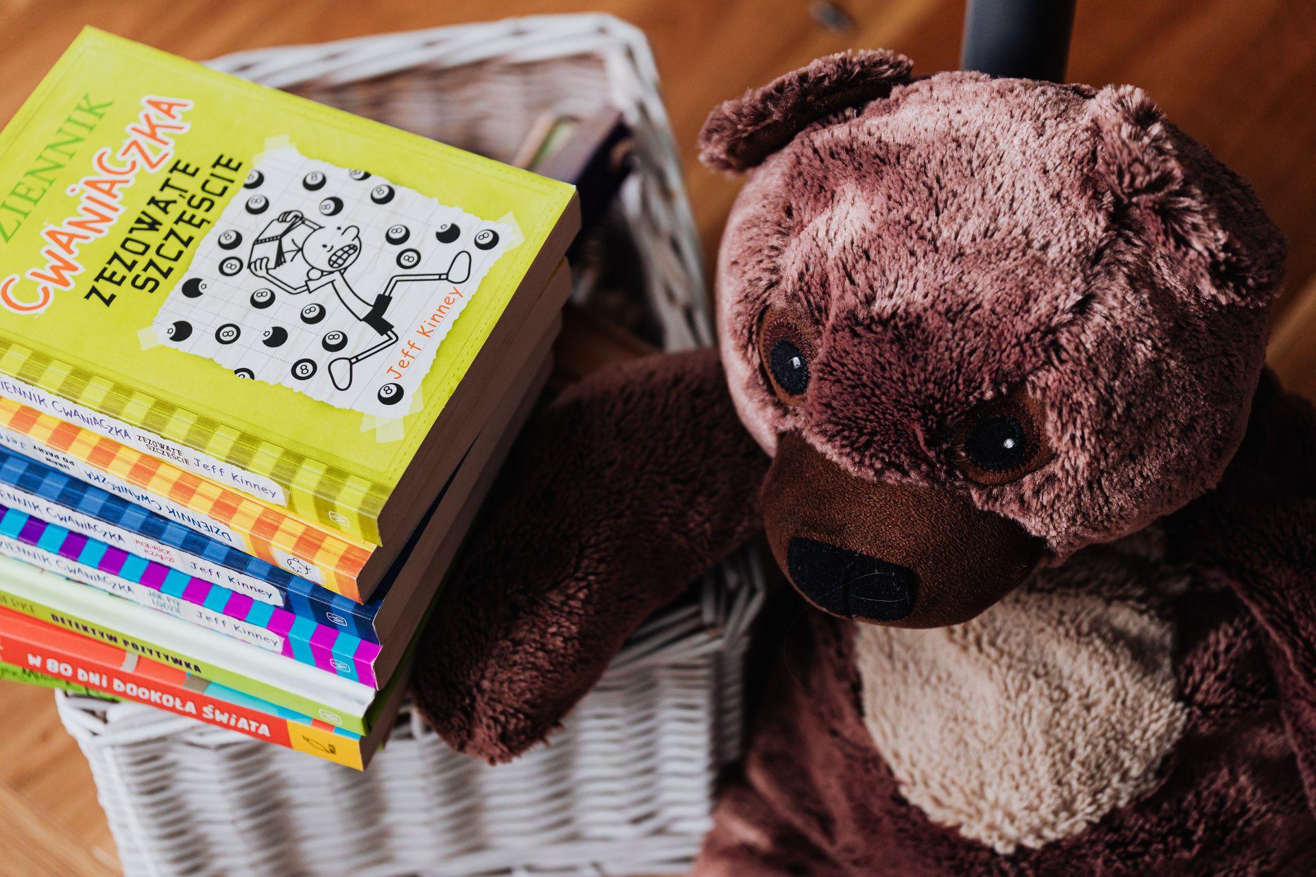 Pilha de livros infantis coloridos ao lado de um ursinho de pelúcia
