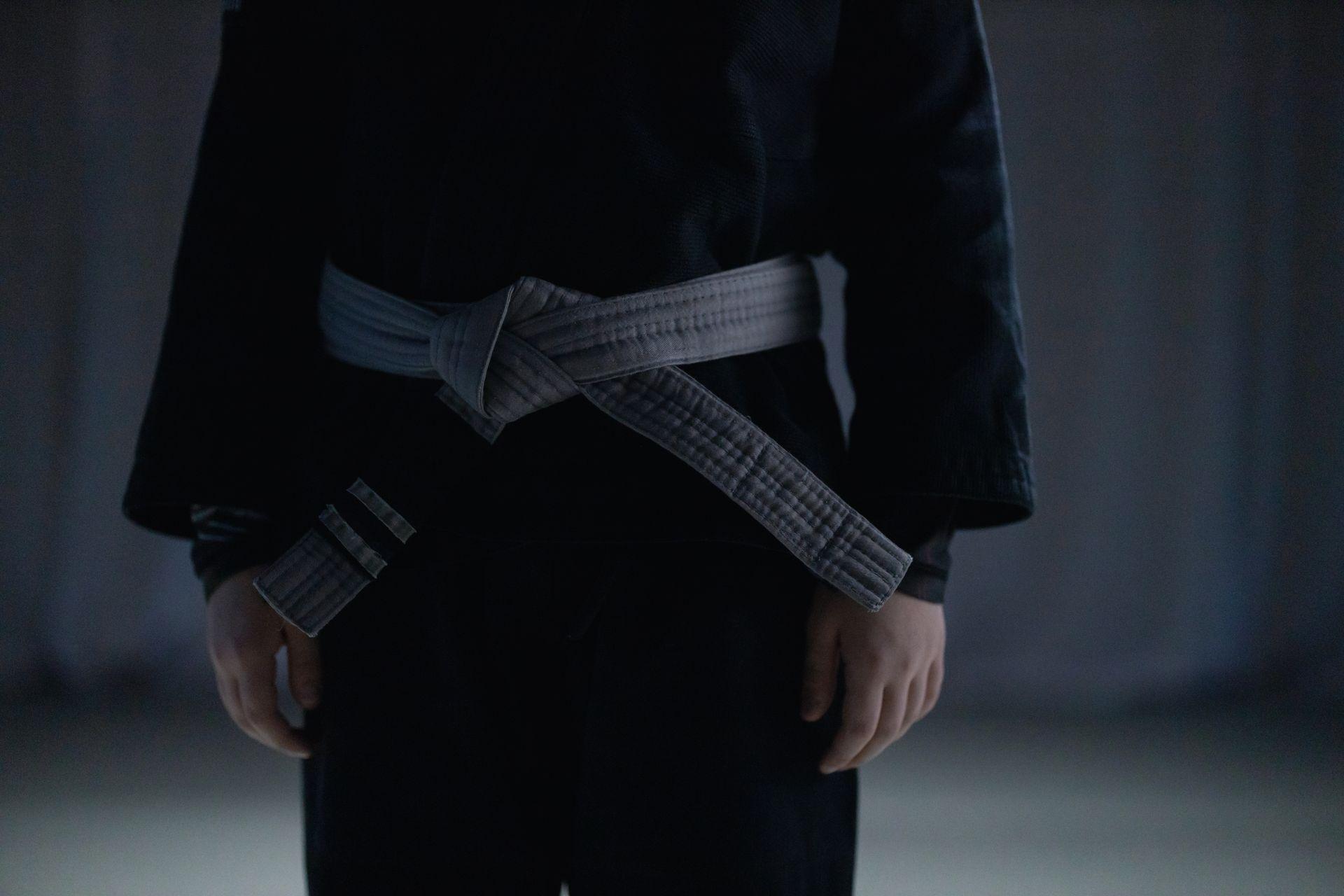 Judoca de quimono preto com faixa cinza, sem o rosto aparecer