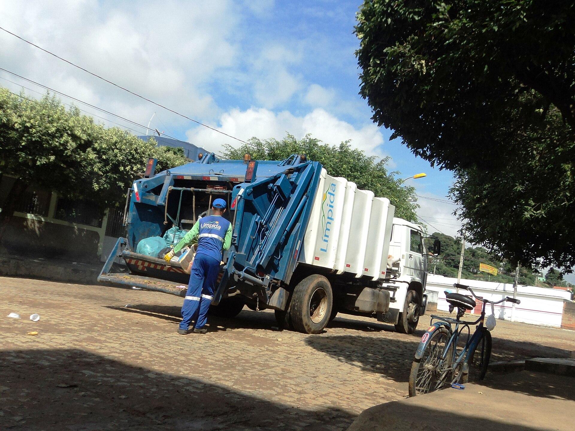 Coletor de lixo de costas ao lado de caminhão de coleta numa rua