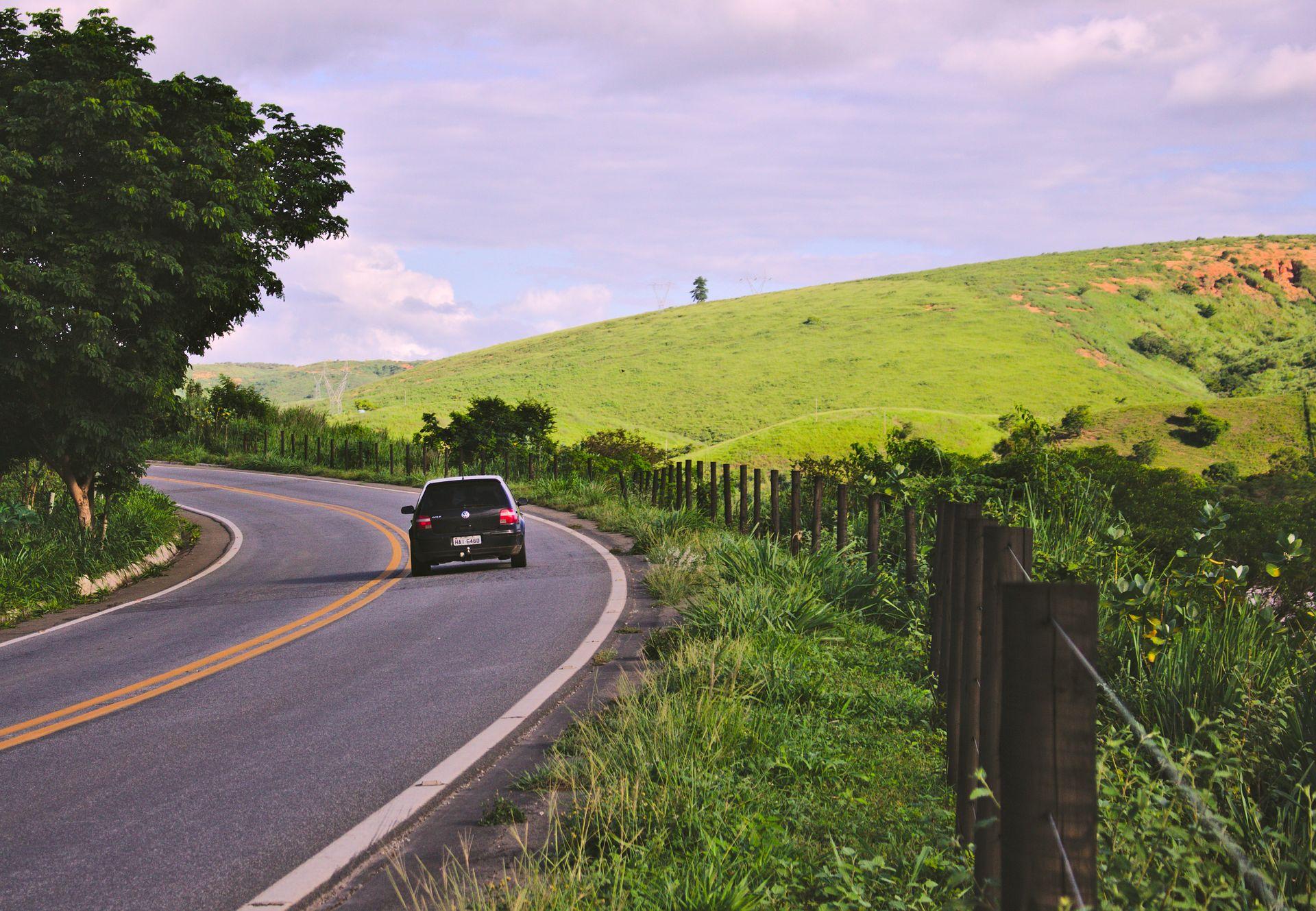 Rodovia de pista simples com curva entre morros verdes e um carro